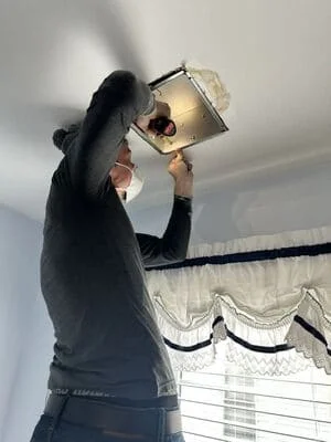 Electrician installing recessed ceiling light fixture into drywall ceiling opening