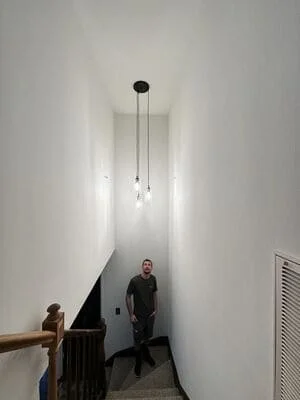 Three pendant lights suspended from black canopy in white stairwell