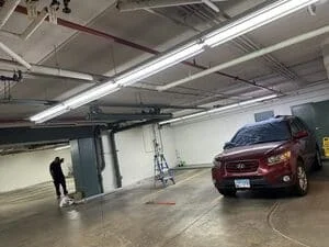 Underground parking garage with overhead electrical conduit, junction boxes, and fluorescent lighting fixtures installed