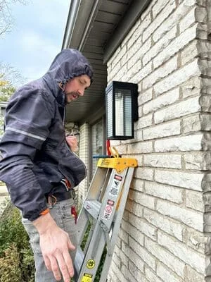 Electrician installing exterior wall light on brick with level and mounting bracket