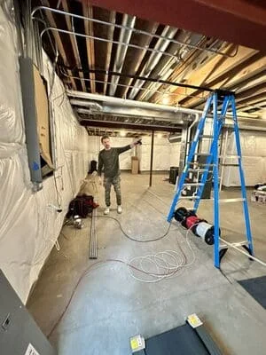 Electrician installing conduit and wiring in commercial space with blue ladder and exposed ceiling
