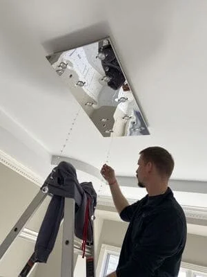 Electrician installing recessed ceiling light fixture with wiring and trim ring