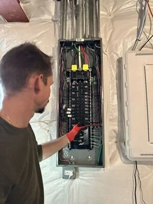 Electrician installing breaker box with yellow conduit wiring and organized circuit connections