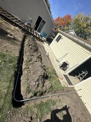 Black PVC electrical conduit trenched along house foundation with metal service entrance box
