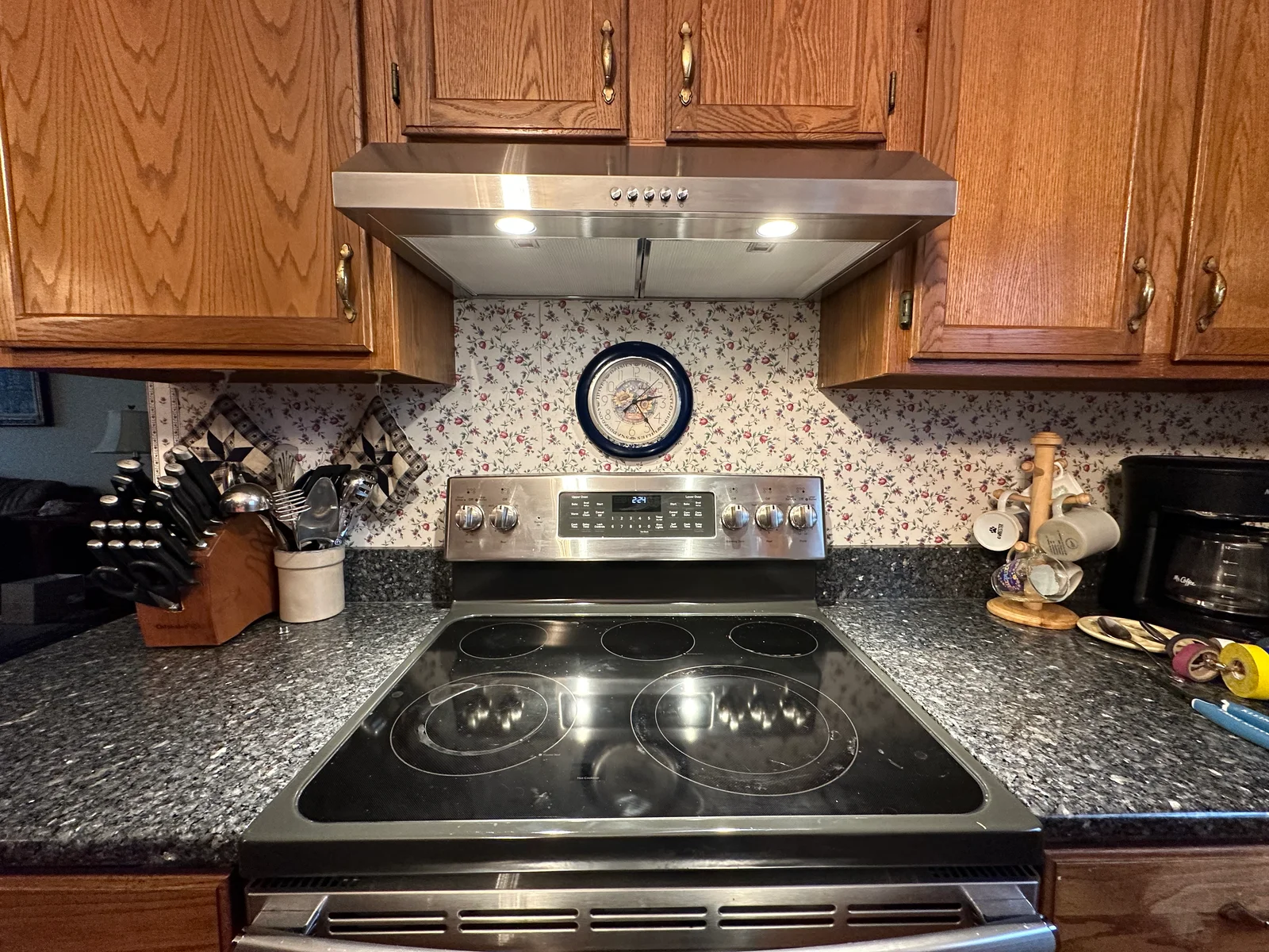 Stainless steel range hood with LED lights installed above electric cooktop with granite countertop