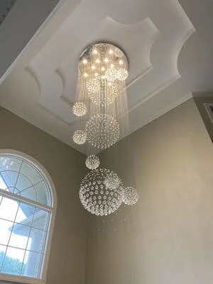 Crystal chandelier with cascading glass spheres installed on coffered ceiling with recessed lighting