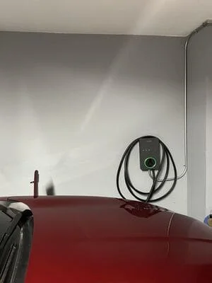 Wall-mounted EV charging station with black cable management above red vehicle