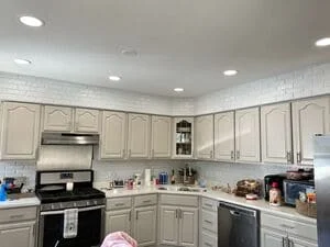 Recessed ceiling lights installed in kitchen with cream cabinets and black appliances
