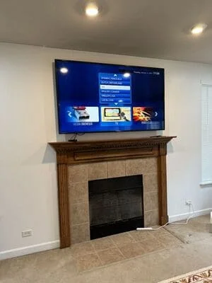 Flat-screen TV mounted above fireplace mantel with recessed ceiling lights and stone fireplace surround
